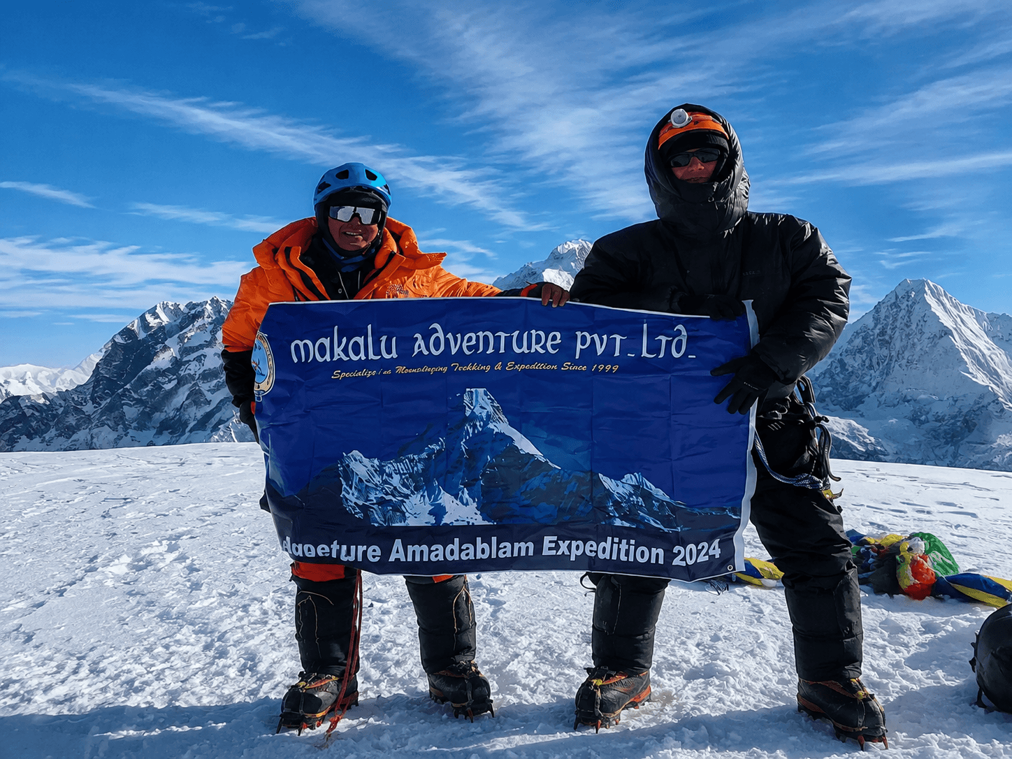Climbers holding a Makalu Adventure expedition banner on a snowy mountain summit.